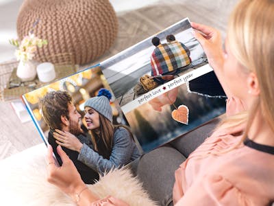 A young woman browsing through a Pixum Photo Book in a square format, designed as a year review.  